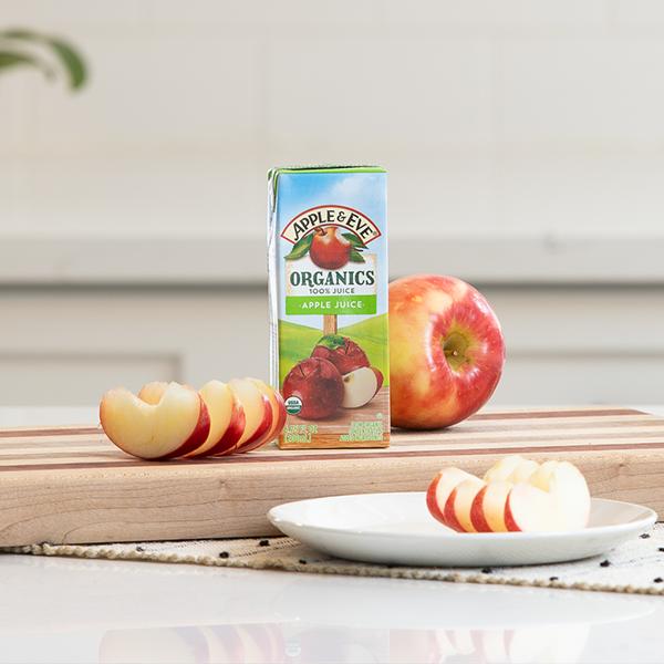 Apple Juice box on table next to fruit.