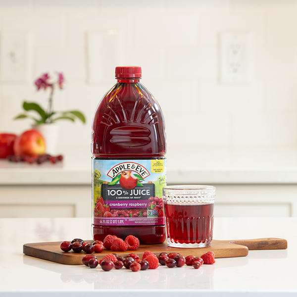 Cranberry raspberry juice bottle sitting on a table next to a glass of fruit and raspberries
