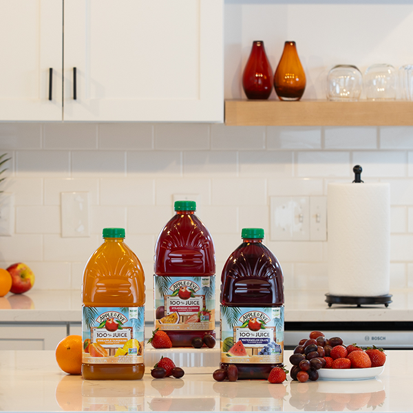 Apple Juice bottles on table next to a bowl of fruit.
