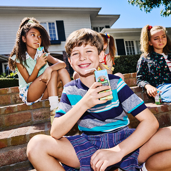 Kids sitting on steps outdoors drinking juice on a warm sunny day.