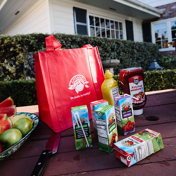 Apple Juice boxes on a table outdoors next to fresh fruit and condiments.