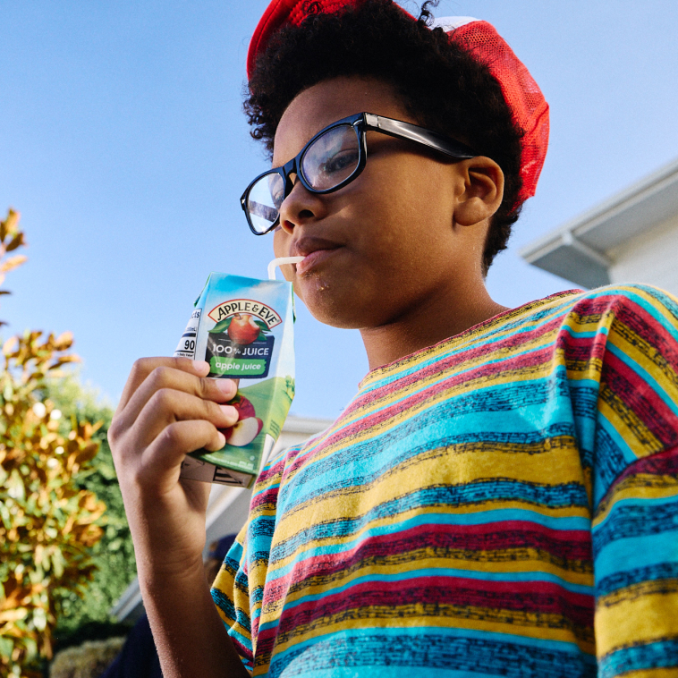 Child with glasses drinking an Apple and Eve apple juice box